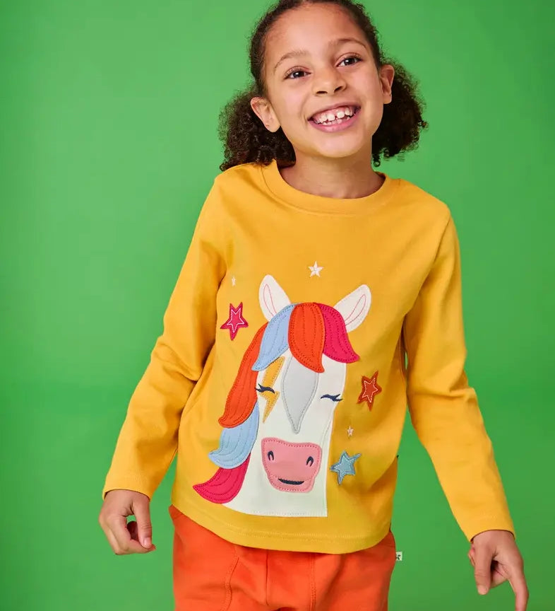 Frugi adventure yellow top with horse and stars applique worn by young girl.