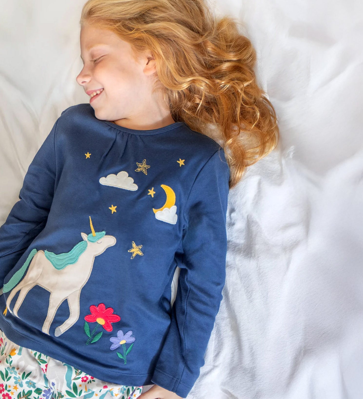 A child wearing the Frugi Organic Cotton Alana navy unicorn forest print children's Pyjamas available at Babipur. 