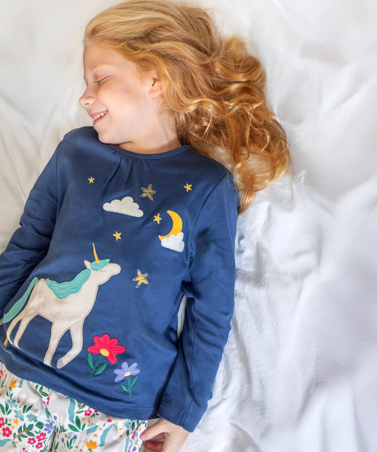 A child wearing the Frugi Organic Cotton Alana navy unicorn forest print children's Pyjamas available at Babipur. 