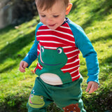 A child playing outside and wearing the Frugi Alfie raglan kids top in red breton frog available at Babipur. A GOTS organic cotton top in red and white stripe with a playful green frog applique on the front.