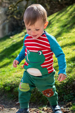 A child playing outside and wearing the Frugi Alfie raglan kids top in red breton frog available at Babipur. A GOTS organic cotton top in red and white stripe with a playful green frog applique on the front.
