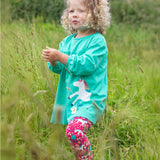 A child playing in a grassy field, wearing the Frugi Tilly Outfit - Pacific Aqua/Wild Horses