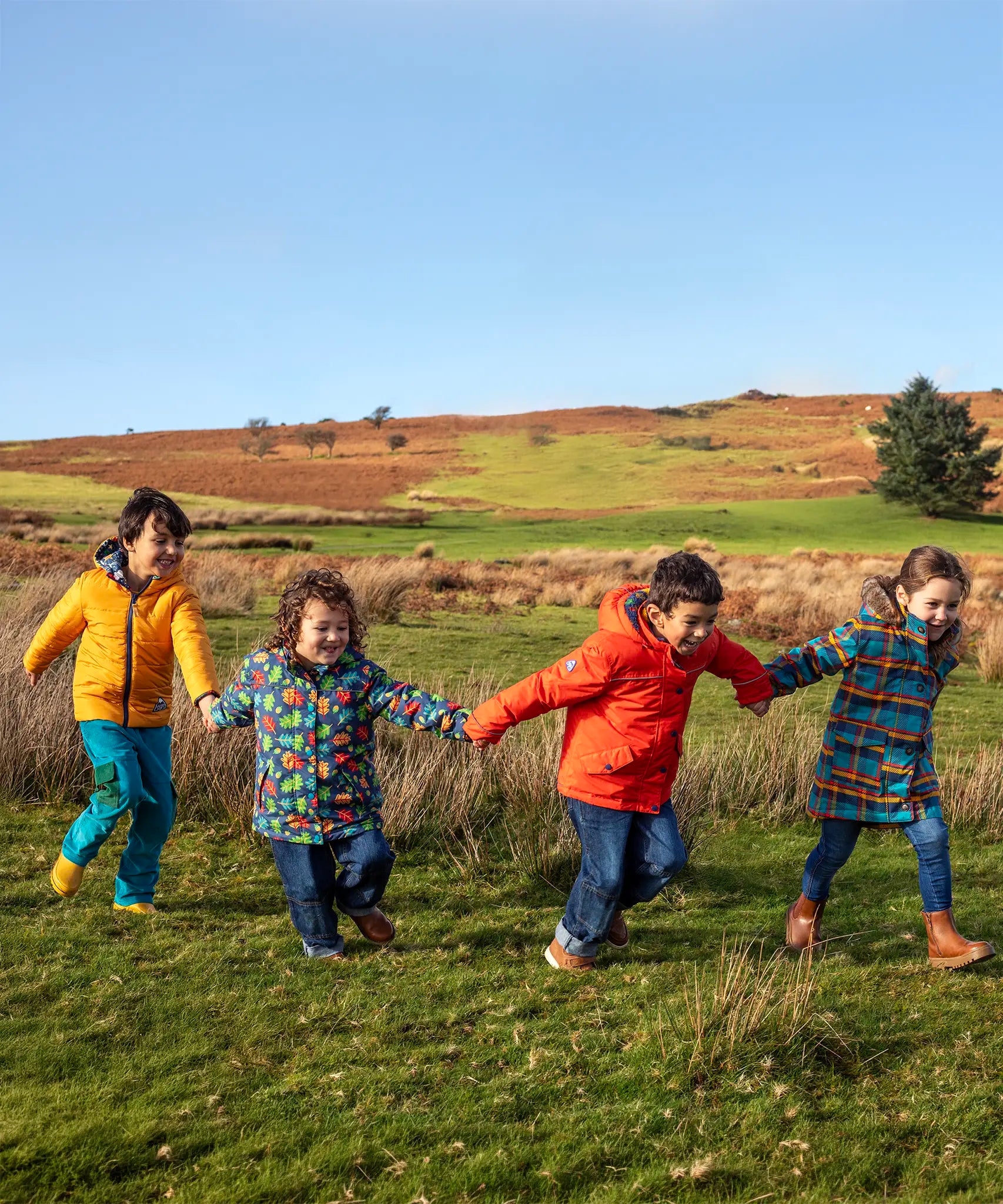 Children in a field and wearing Frugi's reversible, playtime, 3 in 1 rambler and tartan parka coats.