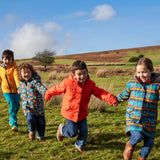 Children playing in a field and wearing Frugi's reversible, playtime, 3 in 1 rambler and tartan parka coats.