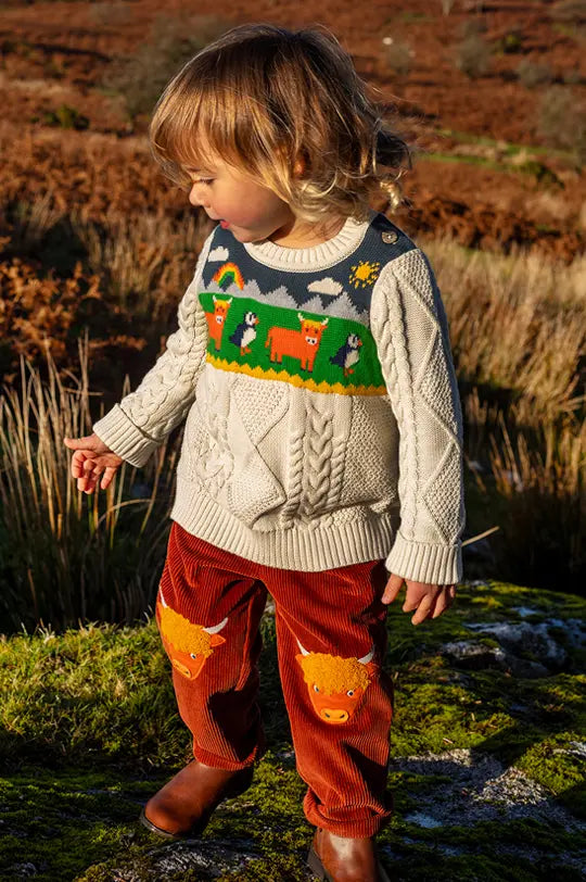 Child wearing Frugi Clyde cable knit jumper and cord Highland cow trousers outside in a field to represent new Frugi at Babipur.