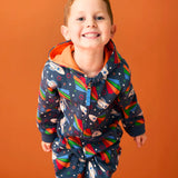 Child wearing Frugi's GOTS organic cotton big hooded snuggle suit in navy with repeating flying rocket prints and a orange inner liner 