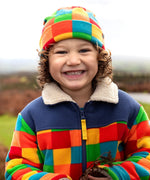 Frugi Blazey Reversible Fleece Jacket in Kaleidoscope rainbow checkered print, worn by child with matching fleece hat.
