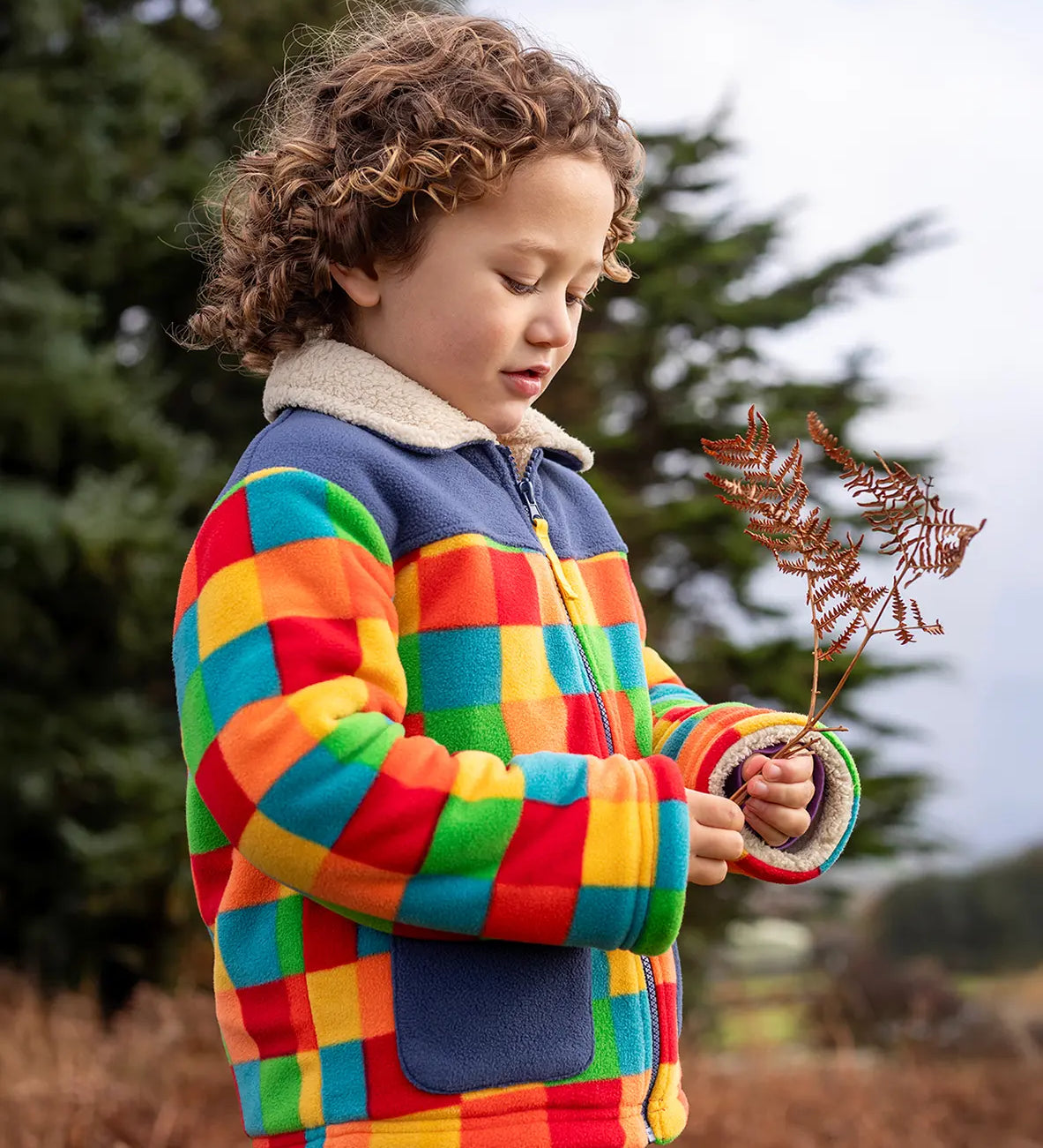 Frugi Blazey Reversible Fleece Jacket with cream collar in Kaleidoscope rainbow checkered print, worn by child with curly hair.