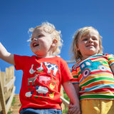 Child wearing Frugi's happy tractor bobster applique t-shirt outdoors next to a child wearing a red tshirt with farm animals