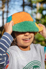 A child standing outside and wearing the Frugi kids fleece bucket hat in hotchpotch and showing the ted fleece detail available at Babipur.