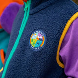 Frugi navy borg fleece gilet with blue and orange piping and 'navigate nature' badge, worn by child with purple hoodie.