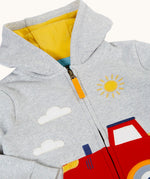 A close up of the light grey Frugi organic cotton hoodie laid flatshowing the zip and the detailing on the red tractor on the bottom
