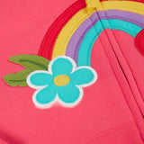 A close up of the light pink zipped hoodie laid flat. Showing the detailing on the rainbow patch and blue flower running across the middle.