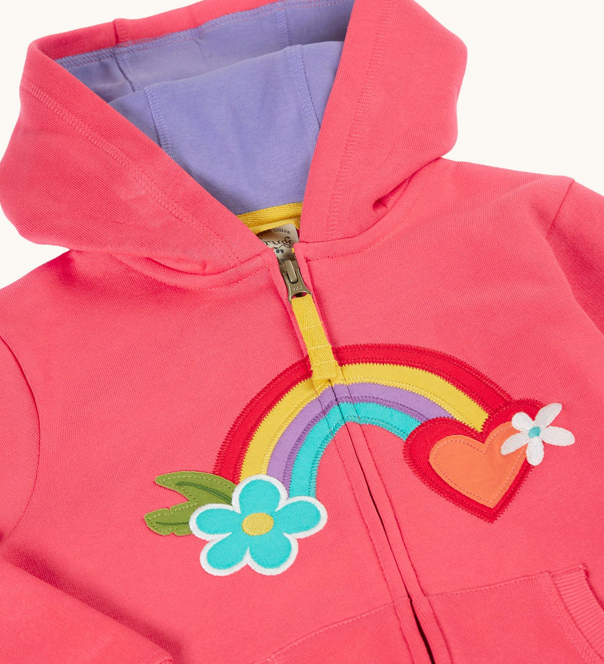 A close up of the light pink zipped hoodie with a light purple inner lining. Showing the detailing on the rainbow patch running across the middle.
