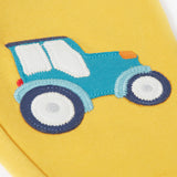 A close up of the bright yellow Frugi joggers laid flat showing the detailing on the blue tractor applique