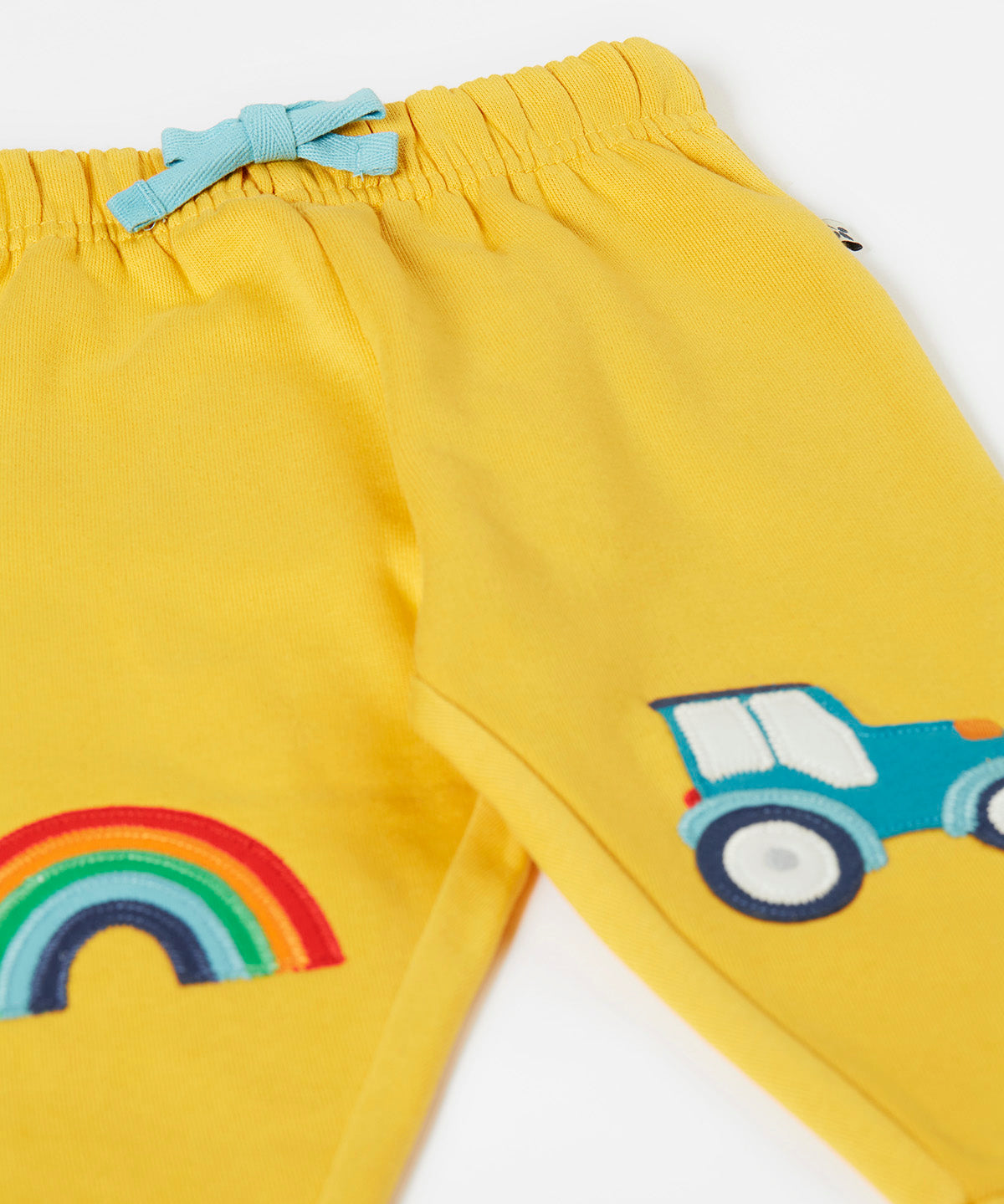 A close up of the bright yellow Frugi joggers laid flat showing the elasticated waist band with a blue tie