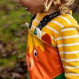Side of child wearing the Frugi waterproof holly green/cow character puddle buster in the forest showing a close up of the Highland cow panel