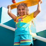 Child wearing Frugi's coast towelling shorts in light blue with red, yellow, blue stripe on hem and holding a skateboard