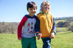 A child standing outside and wearing the Frugi compass kids hooded top in grey bug next to another child wearing the helston reversible hoodie available at Babipur.