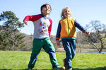 A child walking on grass and wearing the Frugi compass kids hooded top in grey bug next to another child wearing the helston reversible hoodie available at Babipur.