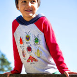 A child wearing the Frugi compass kids hooded top in grey with red raglan sleeve and navy hood available at Babipur. Features various colourful bug appliques on the front panel.