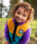 Frugi Cord Fleece Snuggle Suit in Hotchpotch colourblock with 'navigate nature' badge worn by child.