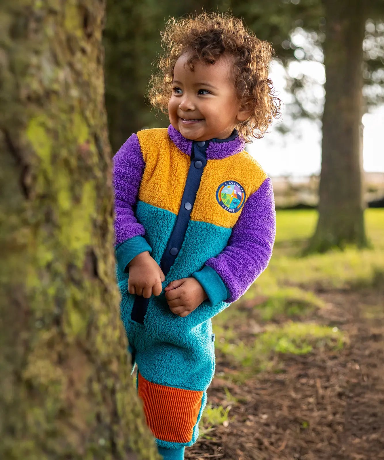 Frugi Cord Fleece Snuggle Suit - Hotchpotch worn by child - a cosy blue, purple and yellow all-in-one with orange cord knee patches.