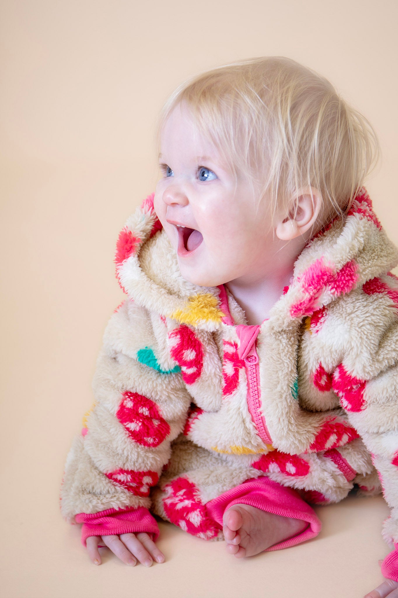 A close up of a toddler wearing the Frugi kids cosy ted snuggle suit in mushroom field available at Babipur, showing the pink zip and cuff trim detail