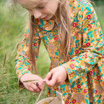 A child wearing the Frugi Autumn Dress - Autumn Friends, and playing with a beetle on their hand
