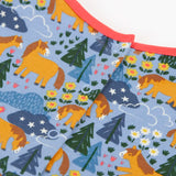 Frugi kids dress in light blue with a playful repeating shetland horse print laid flat showing popper fasteners on the back for easier dressing