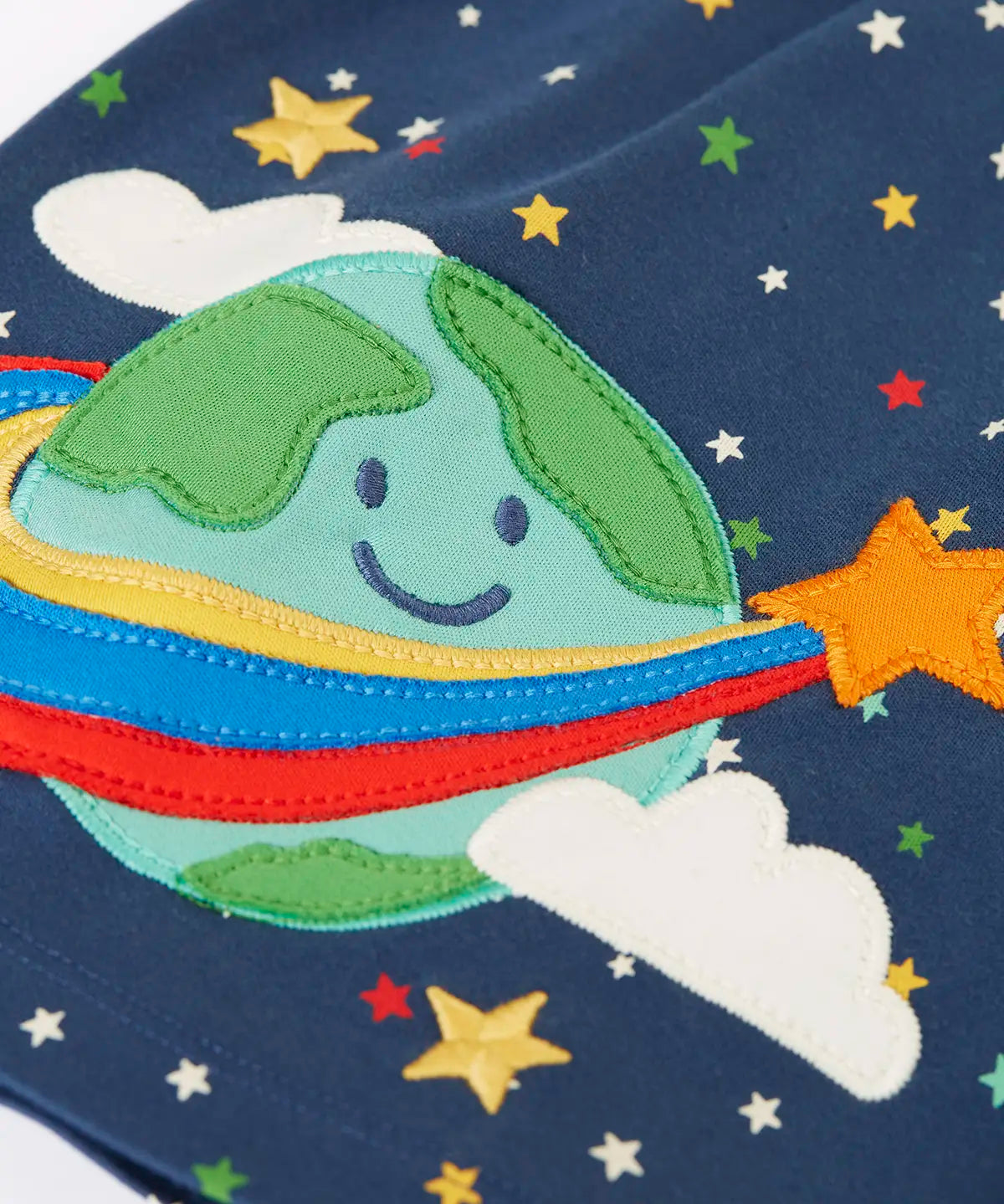 Frugi kids dress laid flat showing close up of the cute planet earth applique on the gather on navy organic cotton fabric