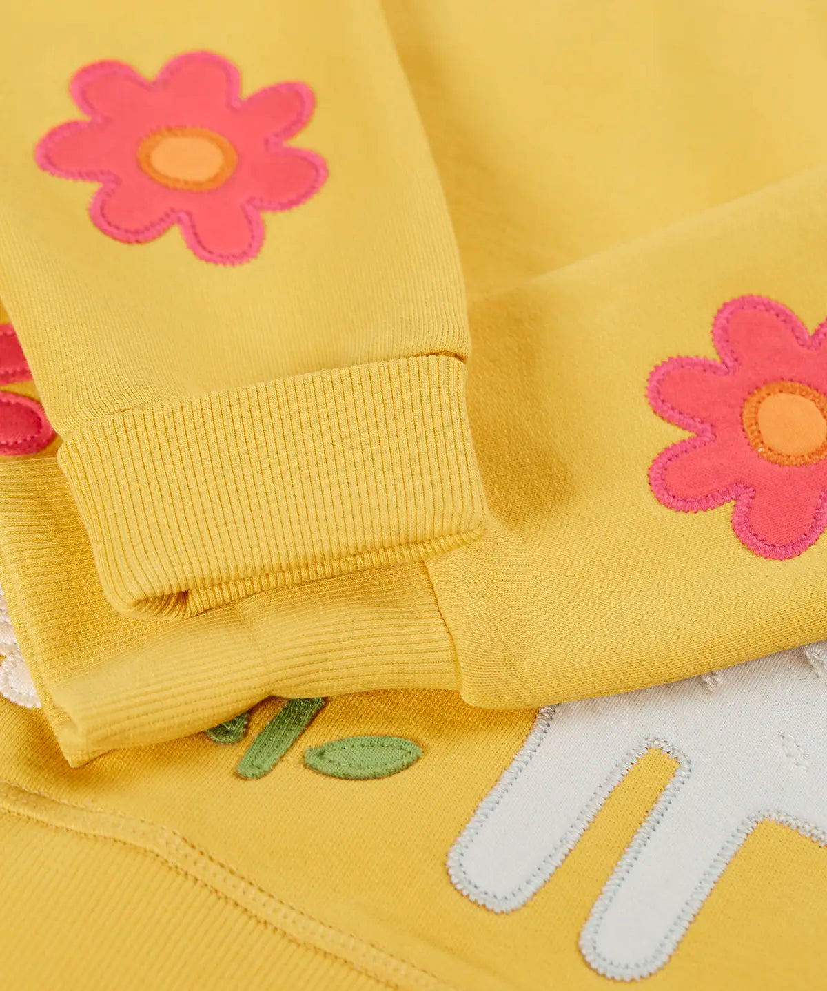 Frugi kids jumper laid flat showing a close up of the cute flower applique on the lower arms on yellow organic cotton fabric