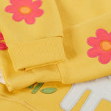 Frugi kids jumper laid flat showing a close up of the cute flower applique on the lower arms on yellow organic cotton fabric