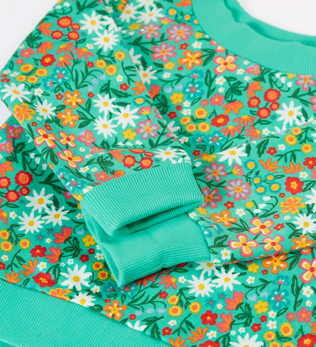 Frugi kids jumper laid flat showing close up of the repeating floral print and elasticated turn up cuffs on green organic cotton fabric