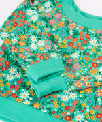 Frugi kids jumper laid flat showing close up of the repeating floral print and elasticated turn up cuffs on green organic cotton fabric