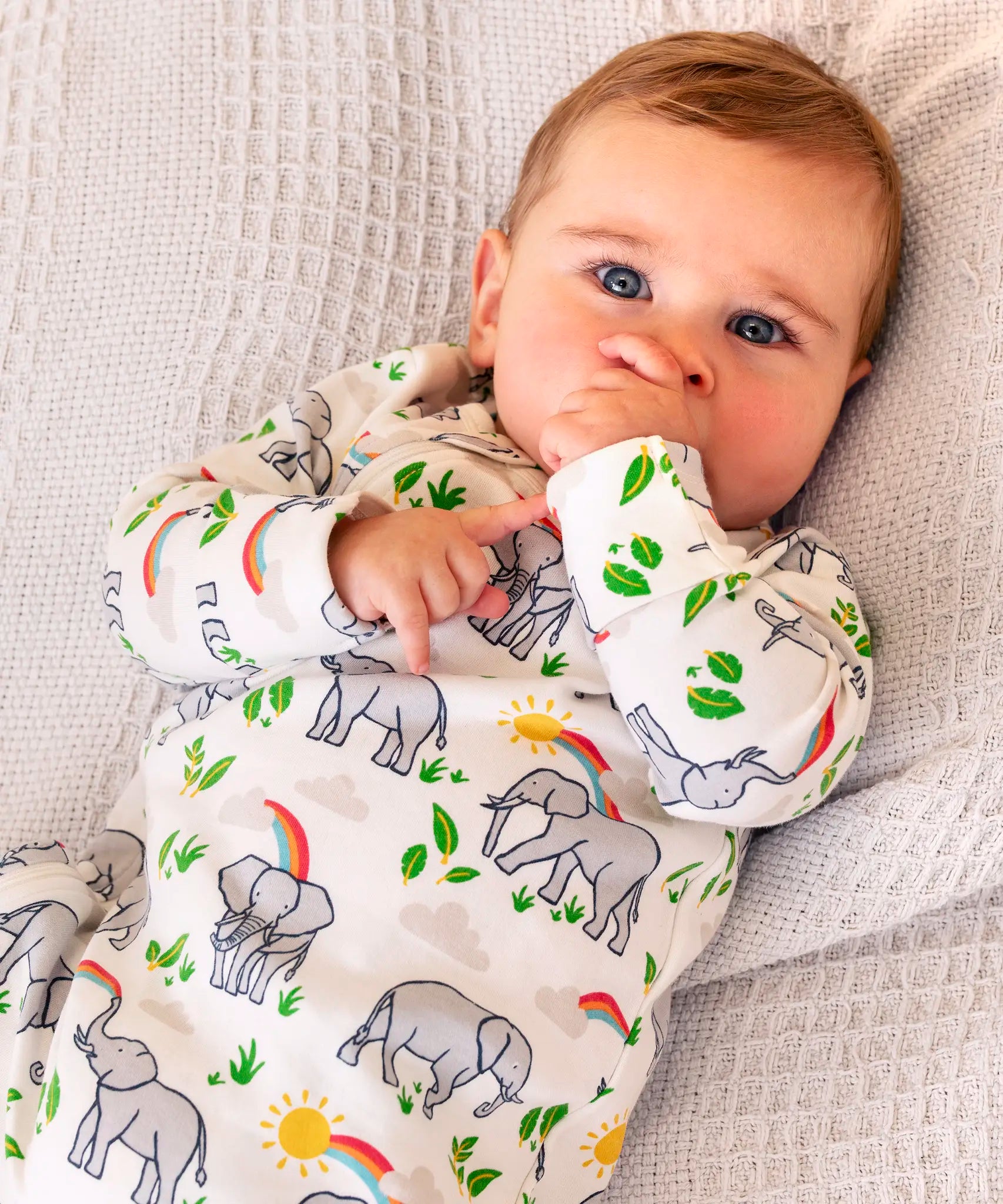 Baby wearing Frugi's white kimono style zipped babygrow with repeating elephant prints