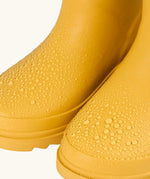Frugi natural rubber, waterproof puddle buster wellingtons in yellow showing close up of the water beading