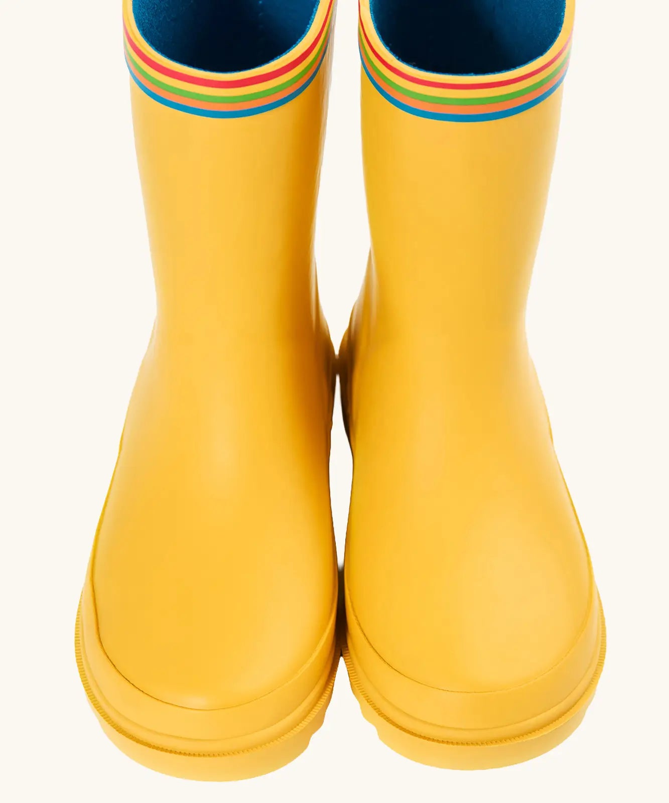 Front of the Frugi natural rubber, waterproof puddle buster wellingtons in yellow showing the rainbow strip on the top and blue inner lining