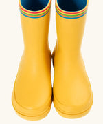 Front of the Frugi natural rubber, waterproof puddle buster wellingtons in yellow showing the rainbow strip on the top and blue inner lining
