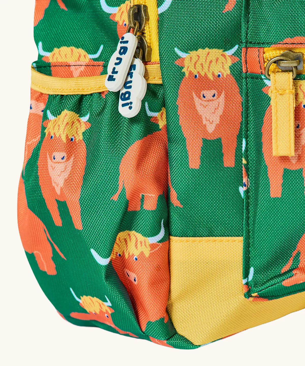 Side of Frugi explorers backpack in green with a repeating highland cow design showing the side pocket