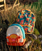 Frugi Highland cow character kids backpack standing next to the explorer  style backpack on a grassy mount