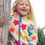 A child happily stood by a tree, wearing the Frugi Zipped Ted Fleece Jacket - Flower Pop