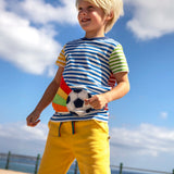 Child wearing Frugi's striped hotchpotch circular t-shirt with a football patch on the front and standing on the promenade
