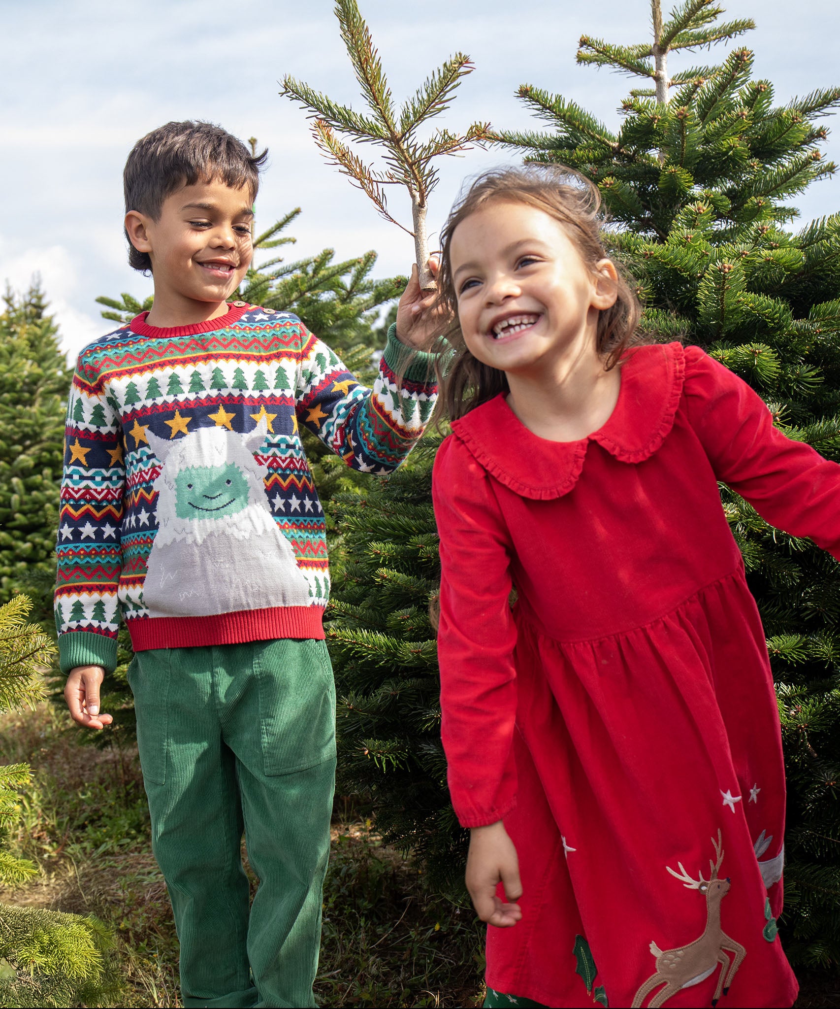 2 children playing in the woods. A boy is wearing the the Frugi forest fairisle/yeti jumper and the girl is wearing the red robin reindeer cord dress.  Both are GOTS organic cotton garments and available at Babipur.