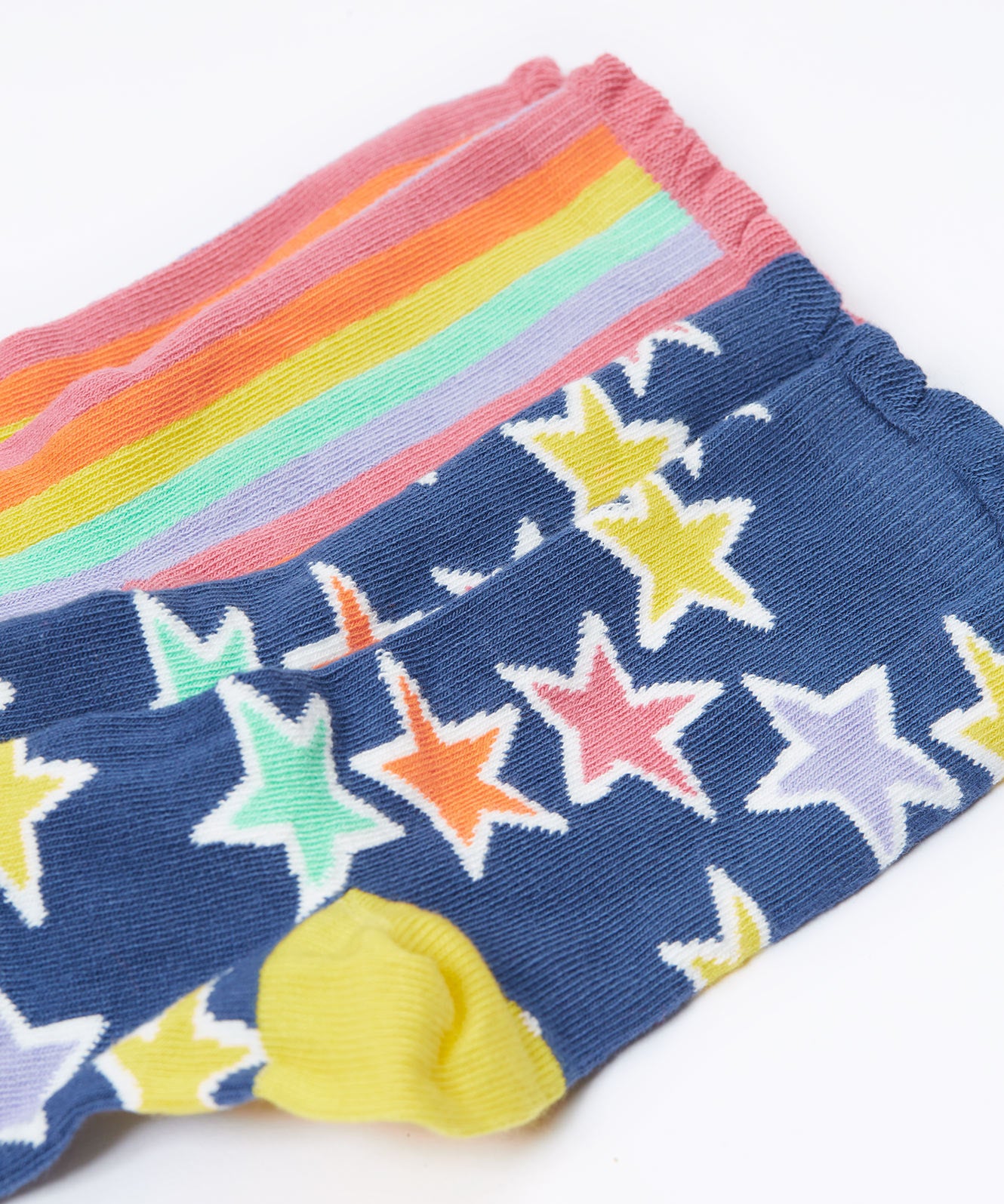 A close up of the blue with bold stars socks from the Frugi Frill Socks 2 Pack in stars available at Babipur. Sock features a gentle frill around the ankle and a yellow heel/toe panel