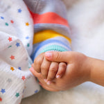 Two children's hands together, with the cardigan and stripes showing in the background