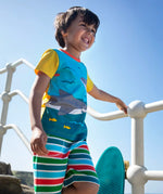 Child wearing Frugi's Iori hotchpotch swimming sharks design with yellow short sleeves t-shirt on concrete stairs