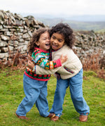 Girls hugging wearing Frugi, Juana Fleece jacket in cream with Alpine Blooms corduroy piping and mouse fairisle cardigans with blue jeans and brown boots.