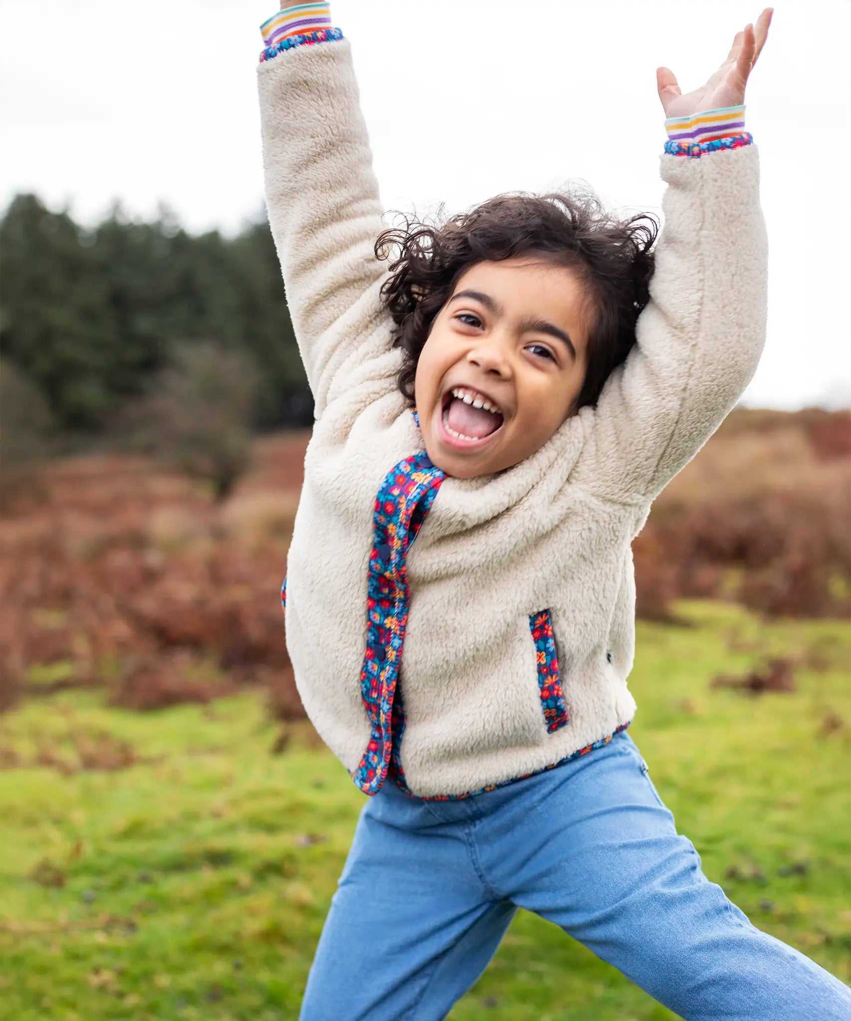 Girl wearing Frugi Juana Fleece jacket in cream with corduroy piping and pocket details in blue floral.