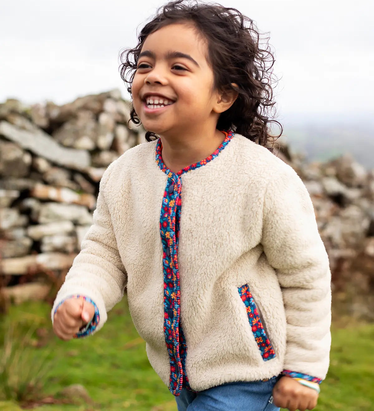 Frugi Juana Fleece jacket in cream with Alpine Blooms corduroy piping, made from recycled polyester, worn by child.